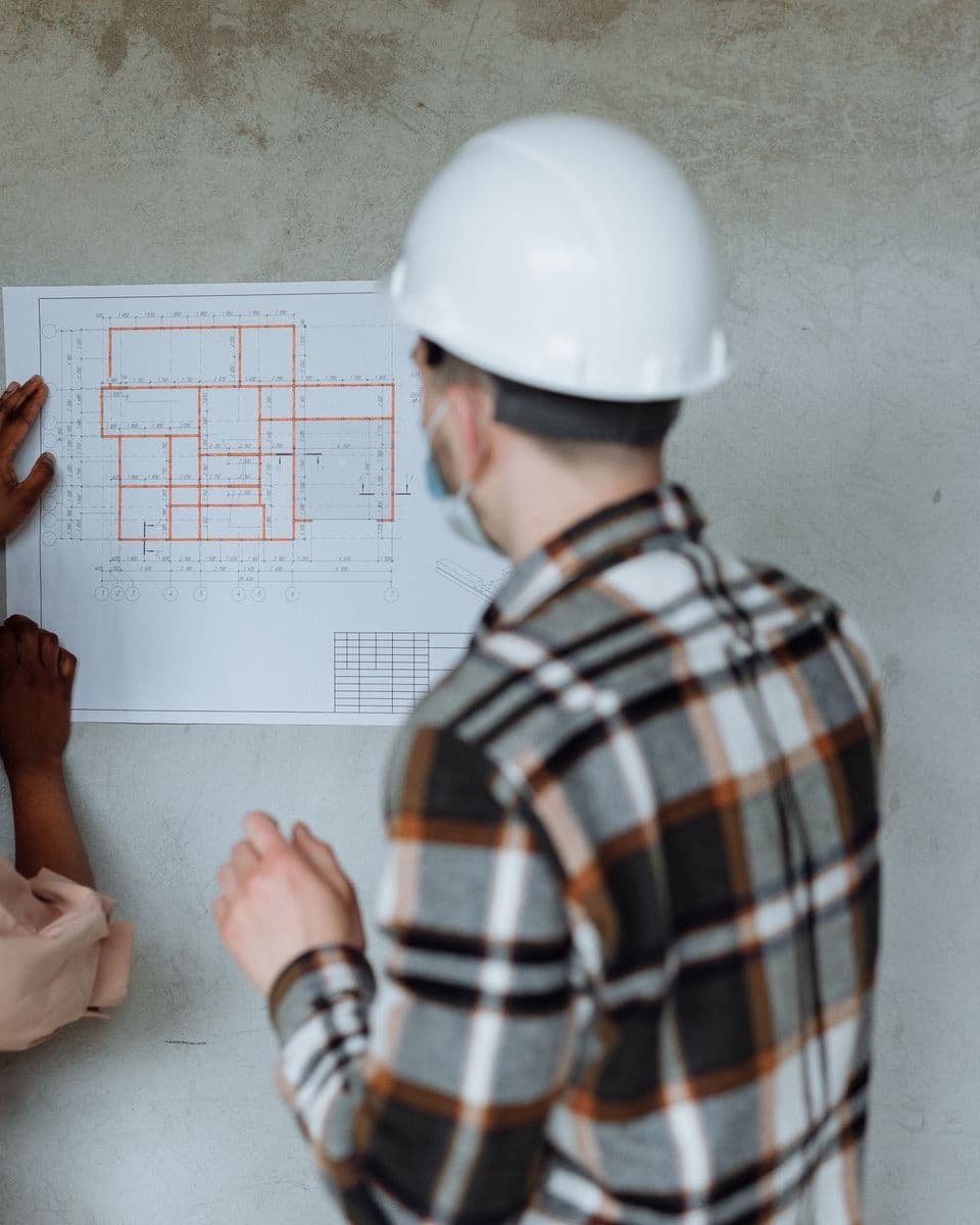 Contractor in a hard hat reviewing a floor plan pinned to a wall