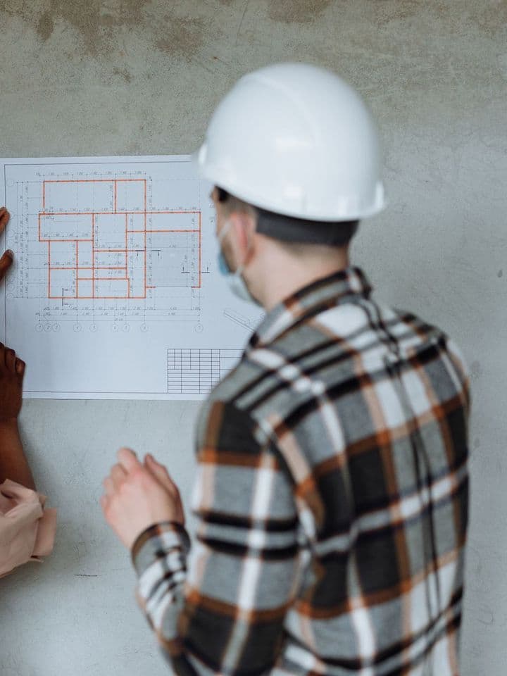 Contractor in a hard hat reviewing a floor plan pinned to a wall