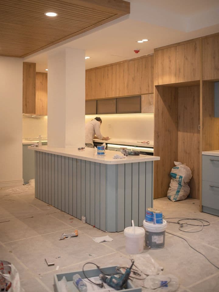 A kitchen renovation in progress with tools on the floor and a worker in the background